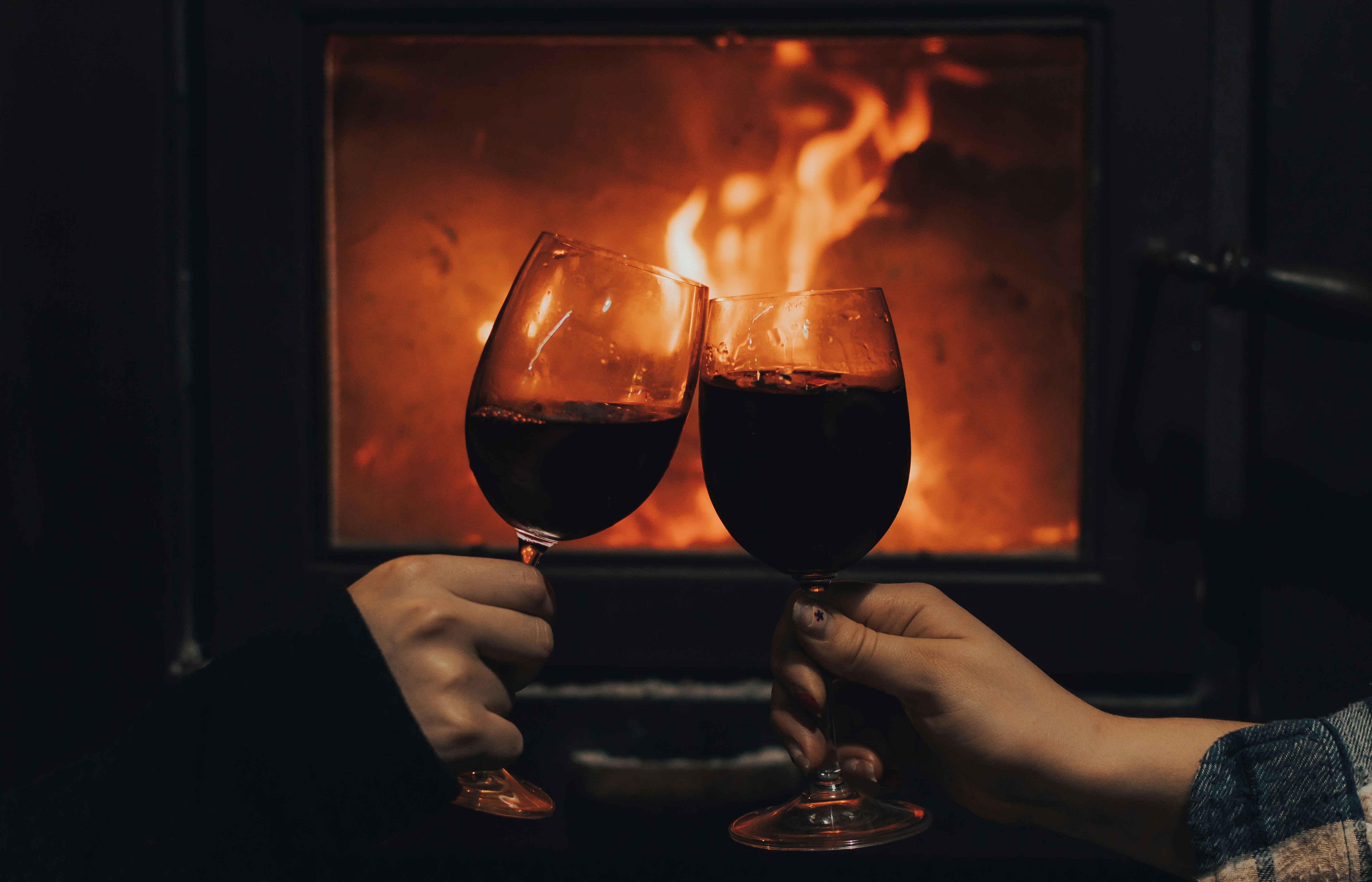 Glasses of red wine clinking beside a roaring fireplace in a cosy chalet setting in Les Arcs, French Alps
